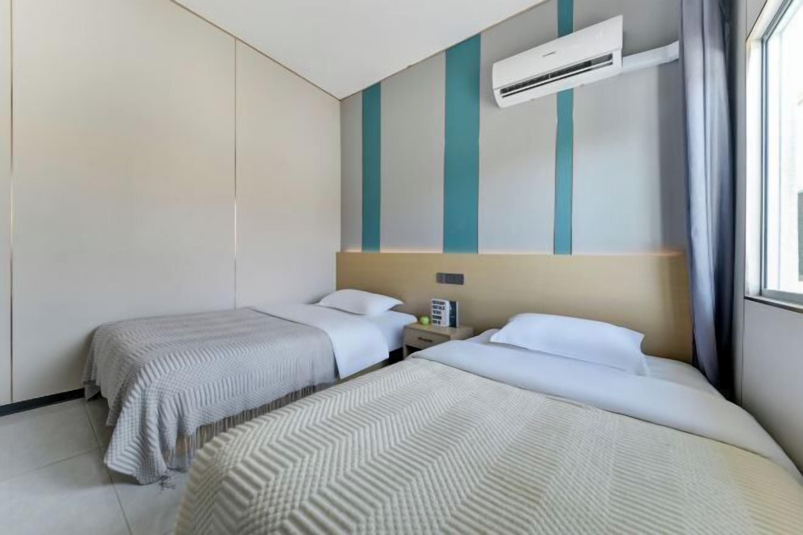 A hotel room with two beds, a nightstand, and an air conditioning unit.