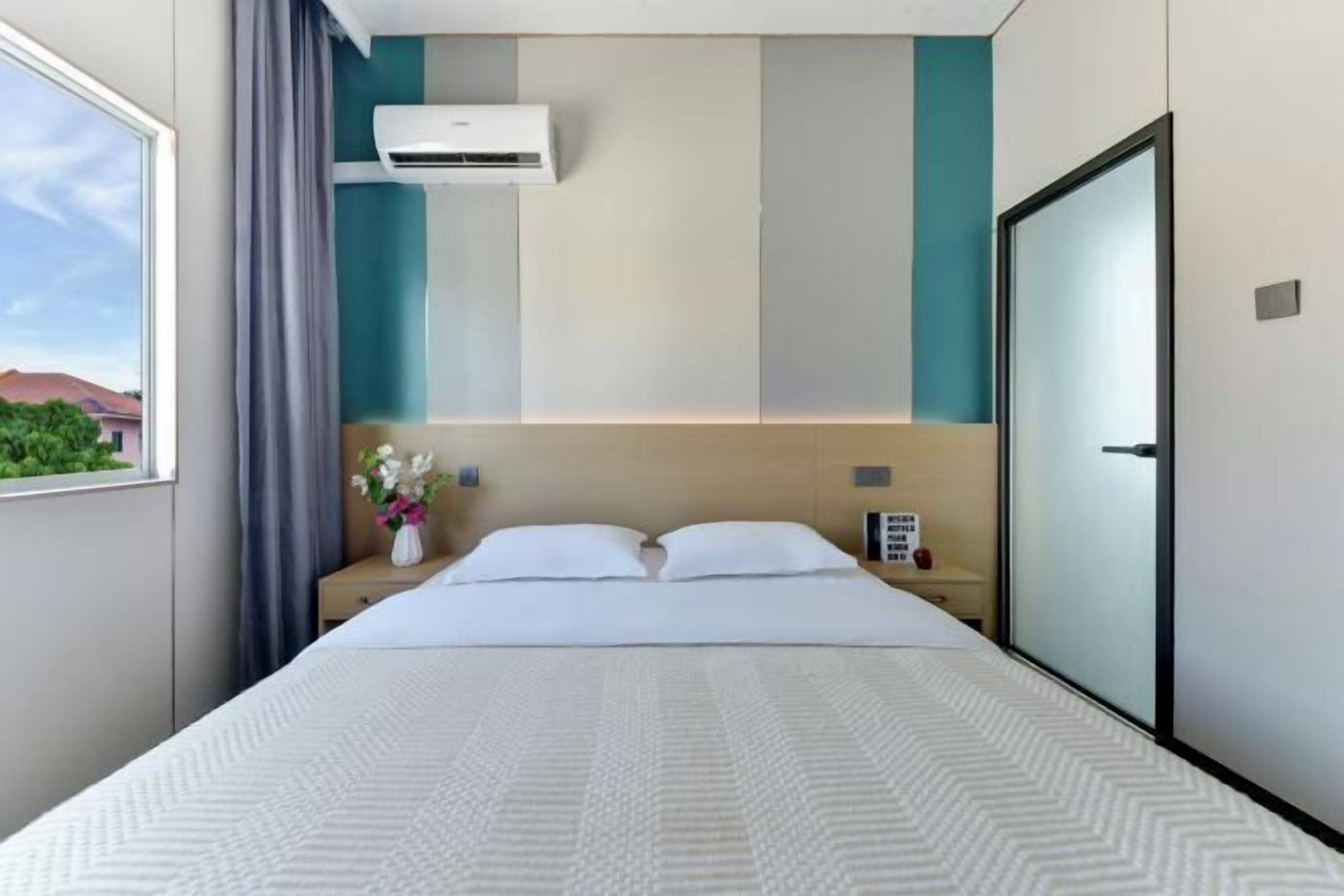 Habitación de hotel con cama, mesita de noche, ventana con cortinas y equipo de aire acondicionado.