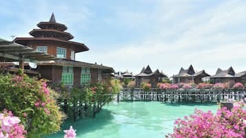 Un resort con bungalows sobre el agua, una edificación central con techo al estilo pagoda y un paseo marítimo de madera sobre aguas cristalinas.
