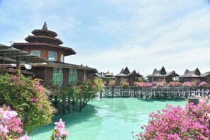 Un resort con bungalows sobre el agua, una edificación central con techo al estilo pagoda y un paseo marítimo de madera sobre aguas cristalinas.