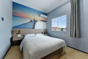 A hotel room with a bed, a nightstand, a window, and a mural of a sunset over water. - Banyan Tree Villa Hotel (Semporna)