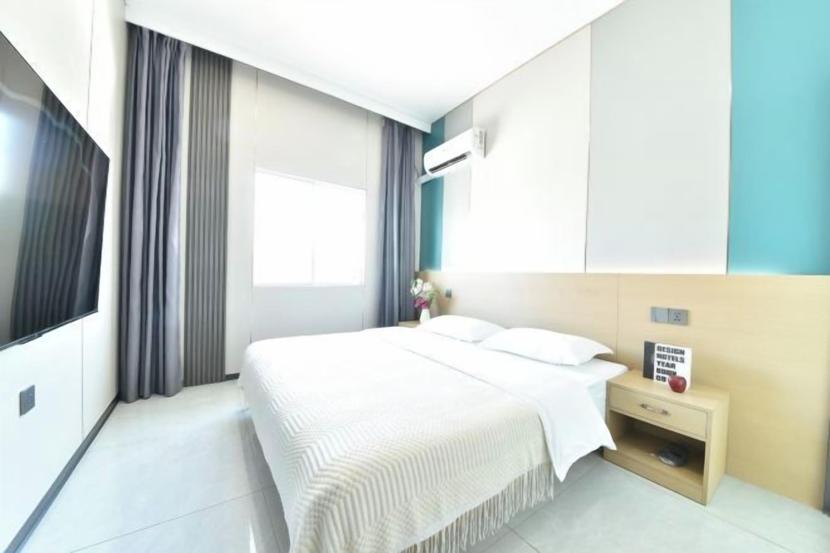 Ett modernt hotellrum med en stor säng, ett sängbord, en platt-TV och ett fönster med gardiner.