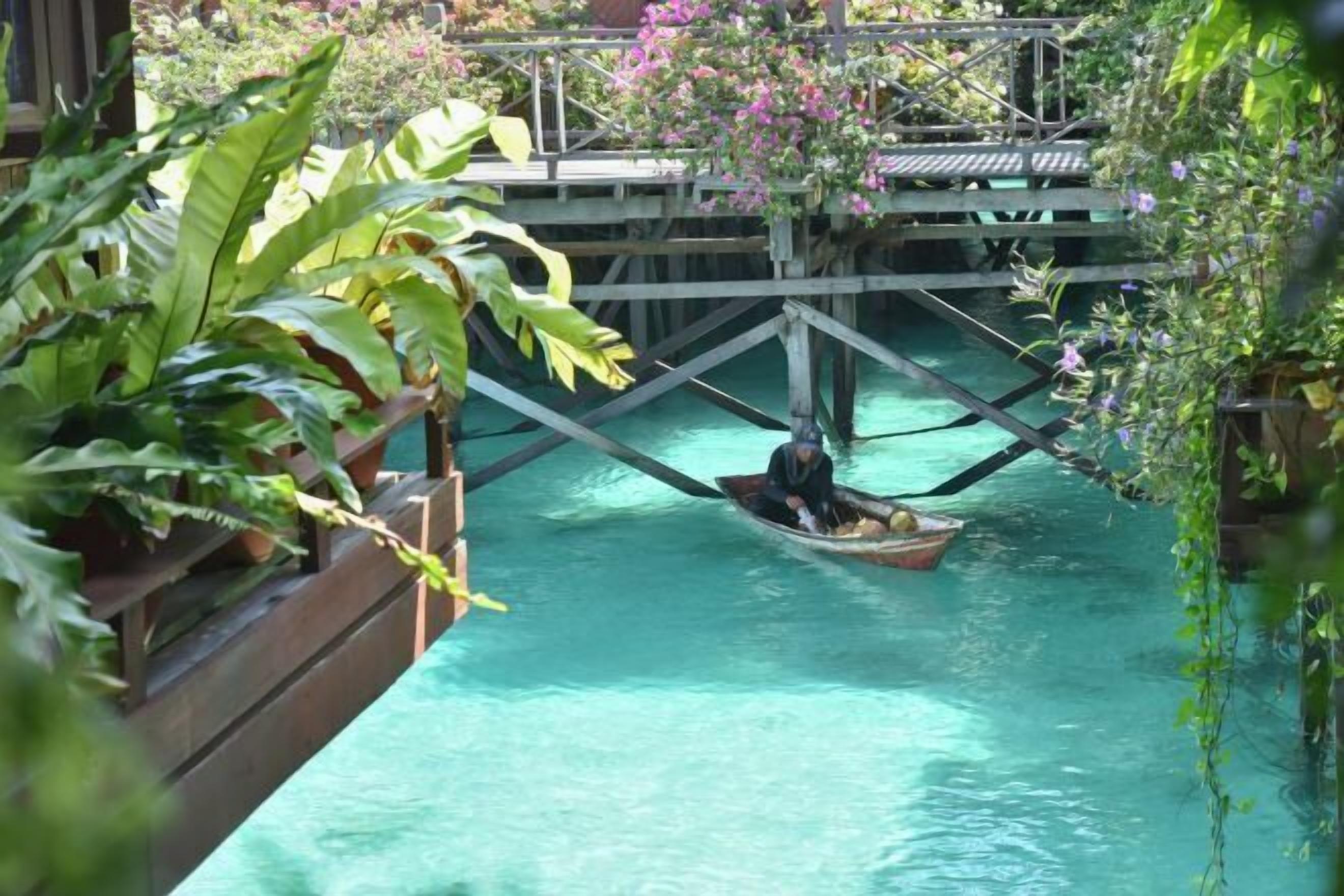 A tranquil waterway with a wooden bridge, lush greenery, and a boat.