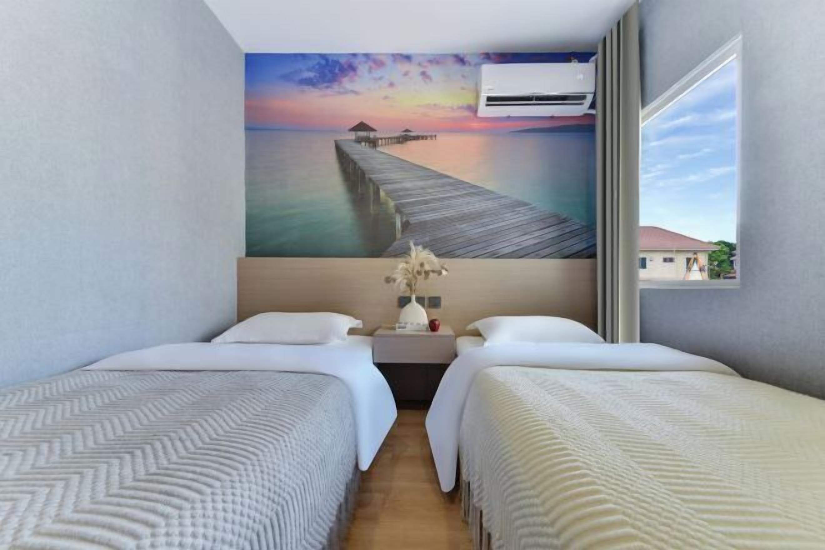 A hotel room with two beds, a painting of a pier, an air conditioning unit, and a window with a view.