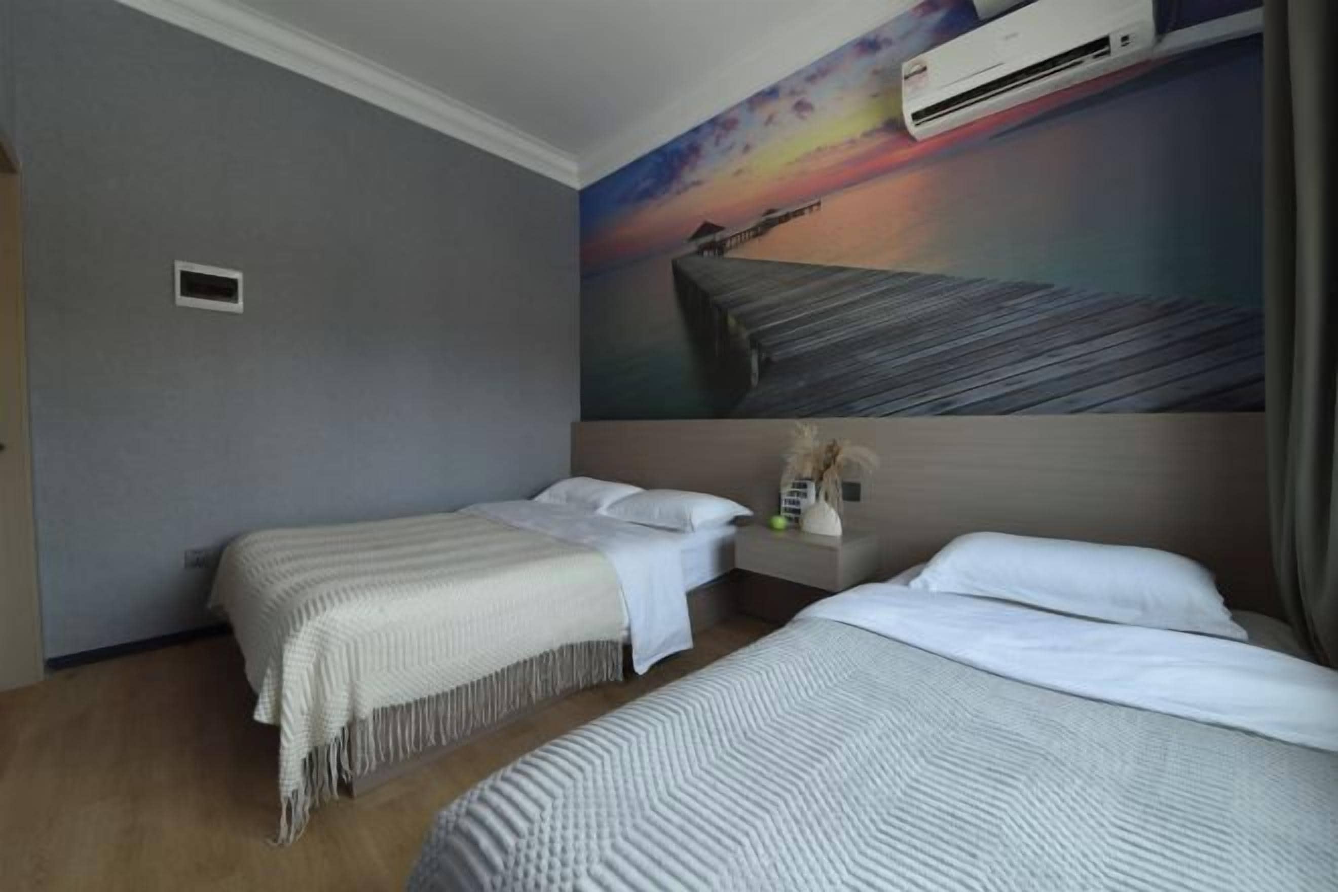 A hotel room with two beds, a painting of a sunset, and an air conditioning unit.
