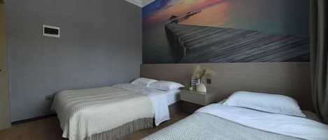 A hotel room with two beds, a painting of a sunset, and an air conditioning unit.