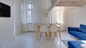 Un salon moderne comprenant un coin repas, un canapé bleu et un téléviseur fixé au mur.