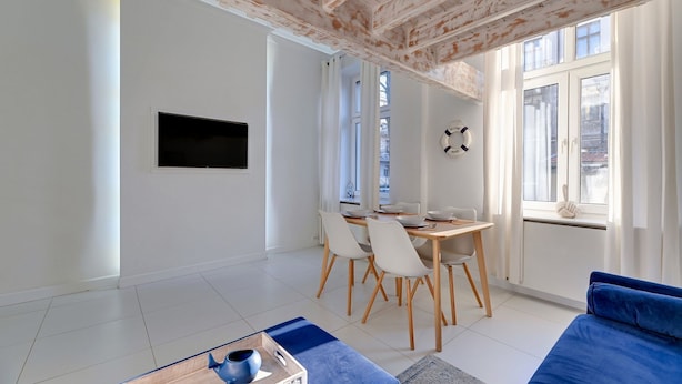 Un salon moderne avec un coin repas, comprenant une grande fenêtre, un téléviseur à écran plat et un canapé bleu.