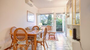 Un coin repas avec un sol à carreaux, des chaises en bois, une table à manger et une vue sur la verdure à l’extérieur.