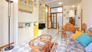 Un salon comprenant un canapé, une table à manger et un téléviseur. On y trouve également des étagères remplies de divers objets et un lampadaire.