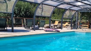 A swimming pool with a glass enclosure, lounge chairs, and a covered patio area. - Le Manoir des Pélies-Au gré du vent. (Conques-en-Rouergue)