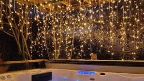 A hot tub with a blue light feature, surrounded by string lights and a view of trees. - Le Manoir des Pélies-Au gré du vent. (Conques-en-Rouergue)