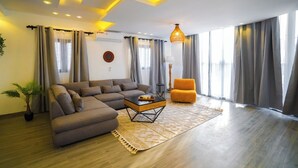 Ein modernes Wohnzimmer mit einem Ecksofa, einem kleinen orangefarbenen Sessel, einem Couchtisch und einem gemusterten Teppich.