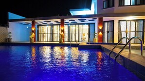 Ein Schwimmbecken mit einem modernen Gebäude im Hintergrund, das große Fenster und einen Poolbereich mit einer Leiter aufweist.