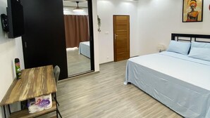 Ein Hotelzimmer mit Bett, Schreibtisch, Stuhl, Fernseher und einer Tür zu einem weiteren Raum.