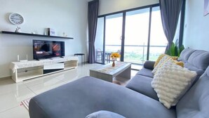 A modern living room with a grey sofa, a flat-screen TV, a coffee table, and a large window with curtains. - Atlantis Residence by Jeffery Lam Home Management (Melaka)