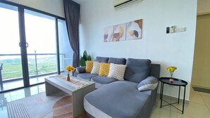 A modern living room with a grey sofa, a coffee table, and a small side table with flowers. There is a large window with a view of greenery outside. - Atlantis Residence by Jeffery Lam Home Management (Melaka)