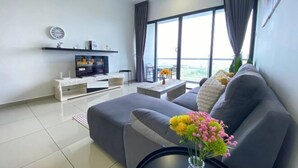 A modern living room with a grey sofa, a flat-screen TV, a coffee table, and a large window with curtains. - Atlantis Residence by Jeffery Lam Home Management (Melaka)