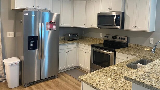 Una cocina moderna con electrodomésticos de acero inoxidable, armarios blancos, encimeras de granito y horno empotrado.
