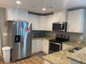 Una cocina moderna con electrodomésticos de acero inoxidable, armarios blancos, encimeras de granito y horno empotrado.
