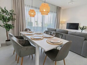 A modern dining area with a white table set for six, grey upholstered chairs, and two woven pendant lights.