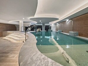 An indoor swimming pool with a curved design, a set of stairs leading to the pool, and a tiled floor.