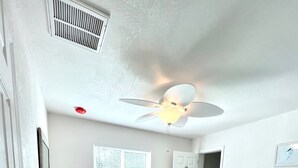 A bedroom with a bed, a ceiling fan, a window, and a door.