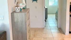 A hallway with a wooden dresser, a wall-mounted ship's wheel, and a sailboat decoration.