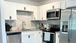 A modern kitchen with white cabinets, stainless steel appliances, a granite countertop, and a tiled floor.