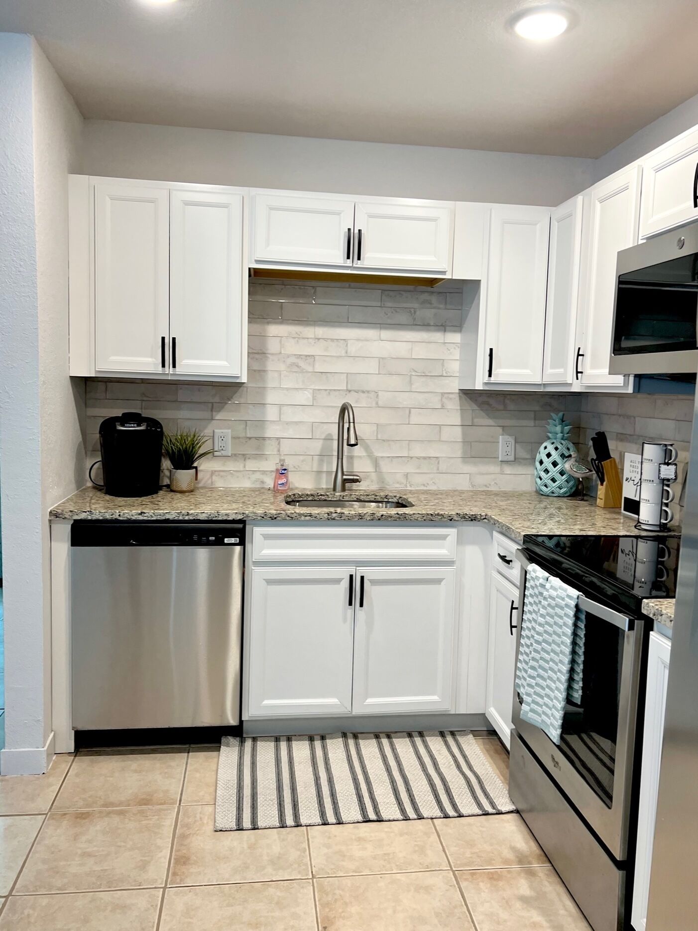 A modern kitchen with white cabinets, a granite countertop, a stainless steel dishwasher, a built-in oven, and a microwave.
