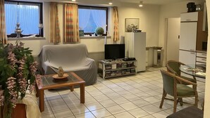 Una sala de estar con sofá, televisor, mesa de centro y un pequeño comedor con sillas.