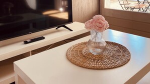 Ein modernes Wohnzimmer mit einem Flachbildfernseher auf einem weißen Schrank, einer Fernbedienung und einer Vase mit Blumen auf einem Tisch.