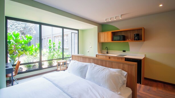 Ett modernt hotellrum med en stor säng, ett litet skrivbord och utsikt över grönområden utanför.