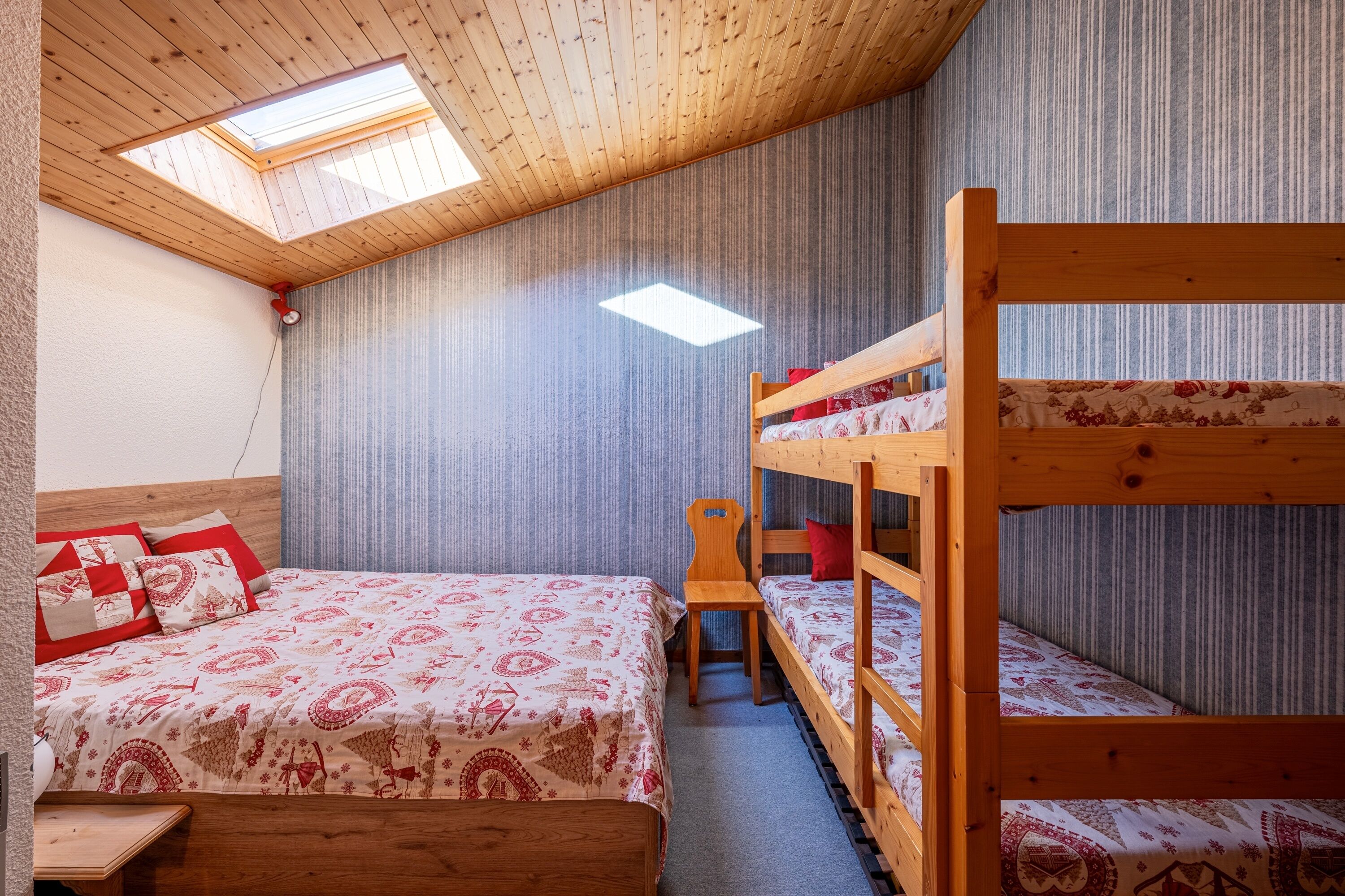 Una stanza con un letto a castello, un letto singolo, un velux e una coperta a motivi.