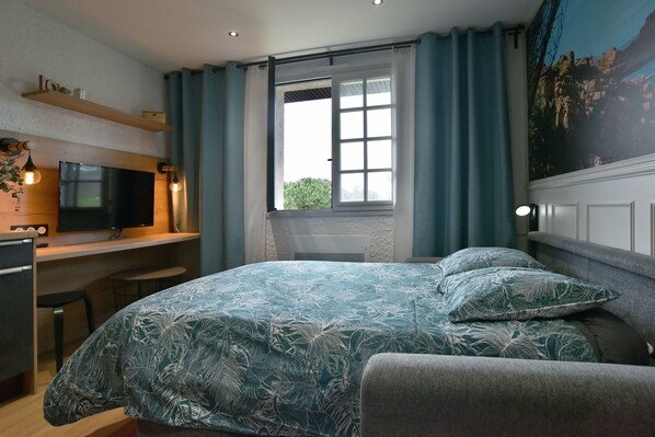 Un dormitorio con cama, escritorio, televisor y ventana con cortinas.