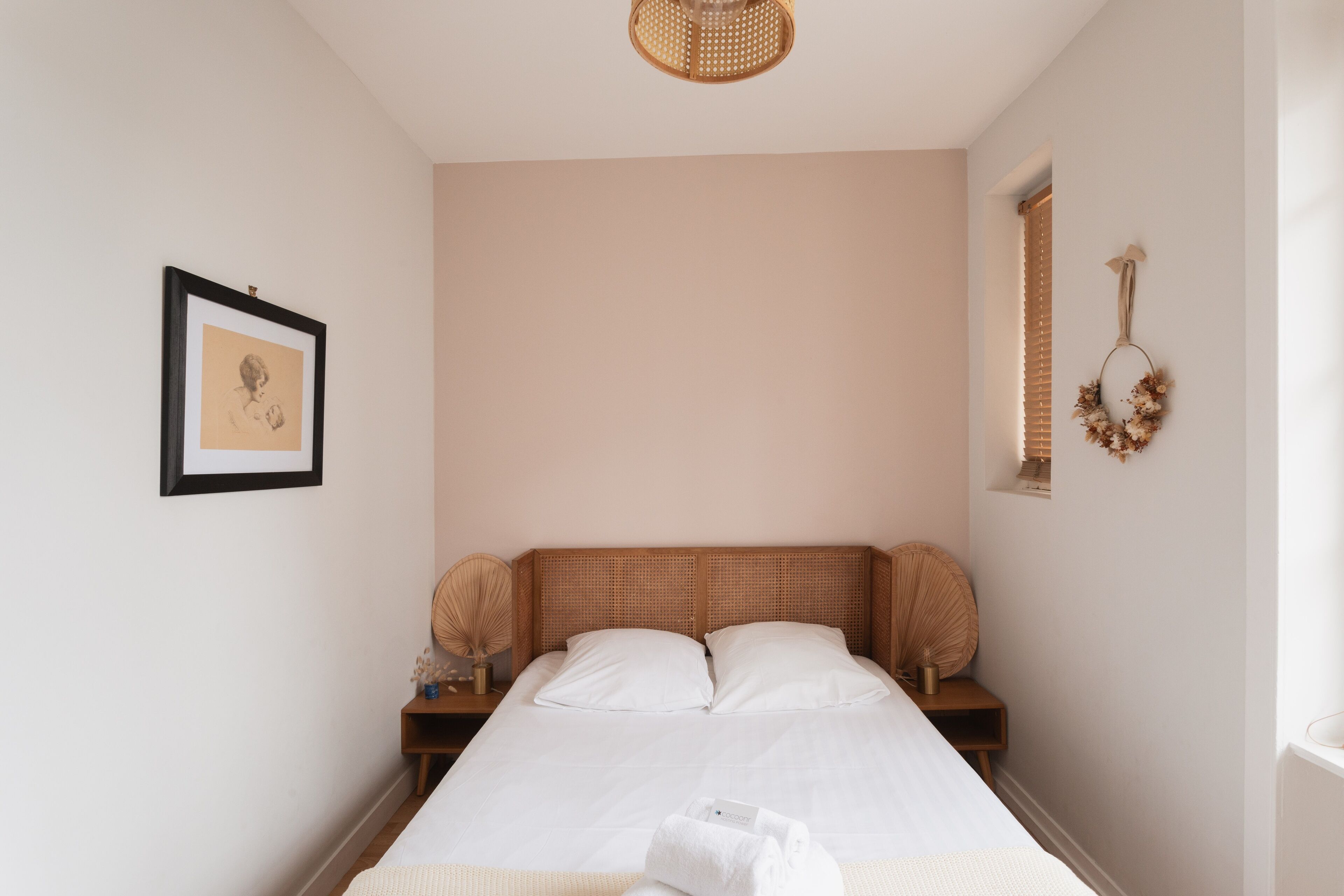Een keurig opgemaakt slaapkamer met een bed, een lijst met een afbeelding aan de muur en een decoratieve krans.