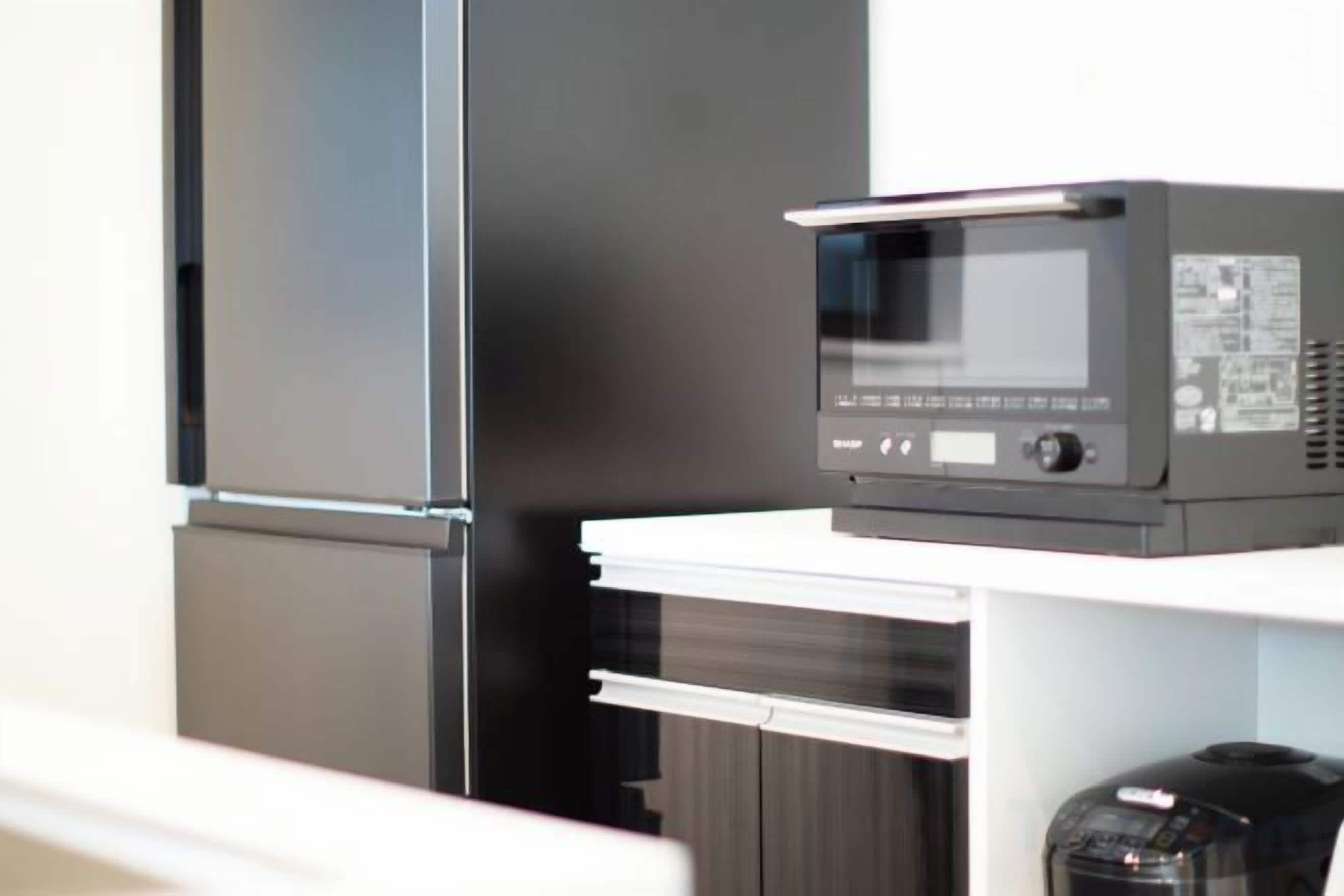 A kitchen with a microwave on a white countertop, a black refrigerator, and a black coffee machine.