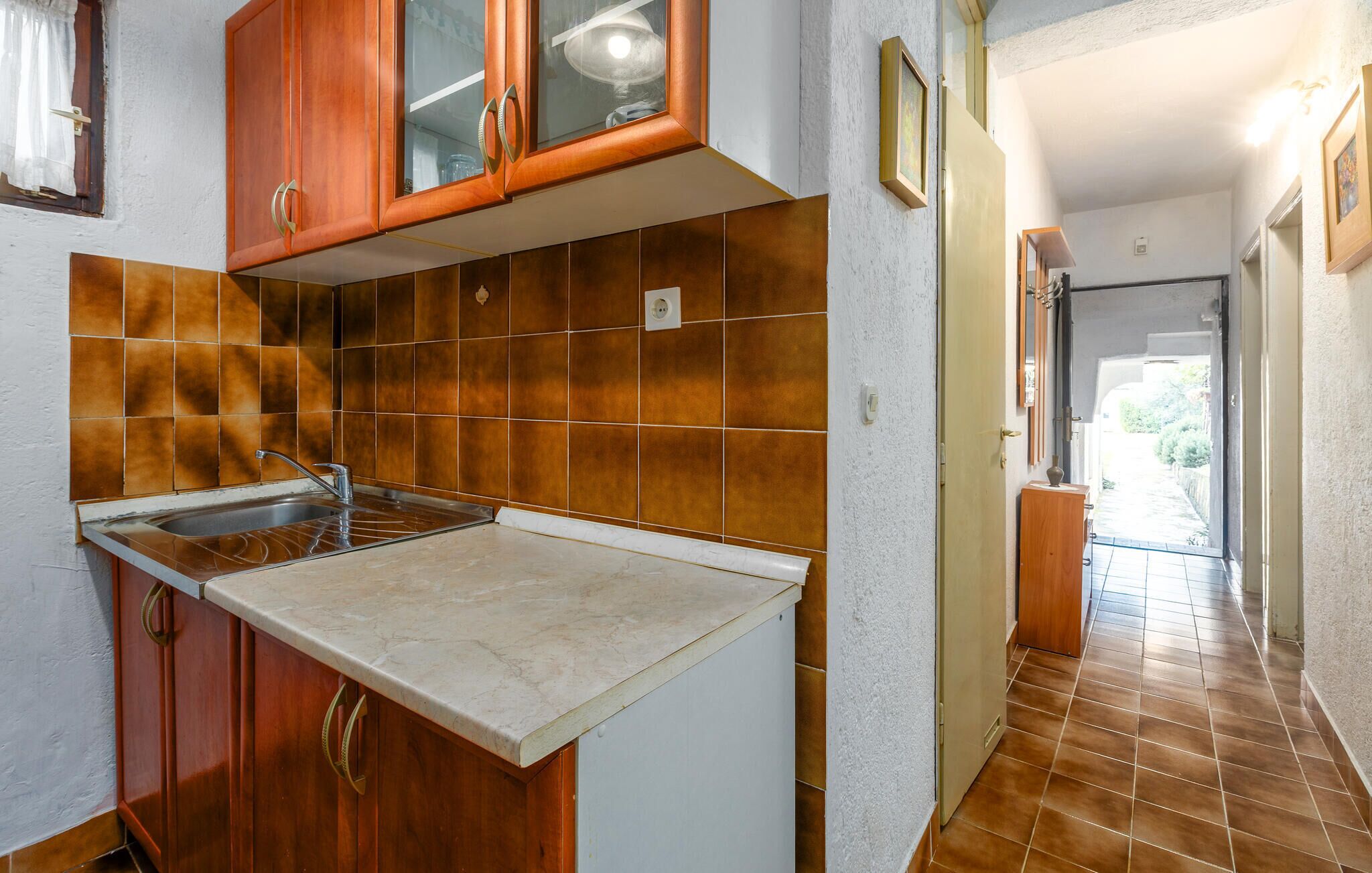 A kitchen with brown tiles, a sink, and wooden cabinets.