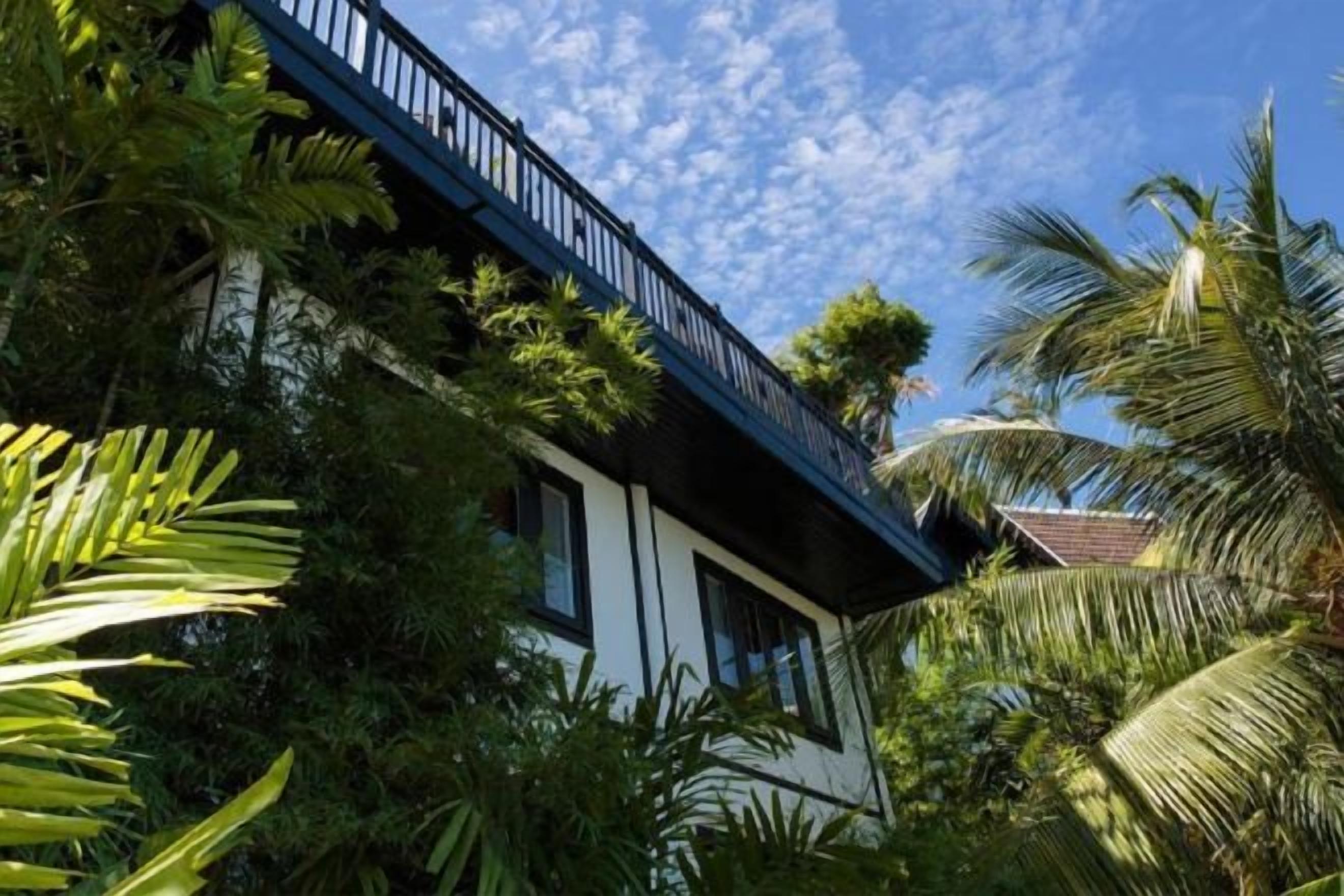 A building with a balcony overlooking lush greenery and a clear sky.