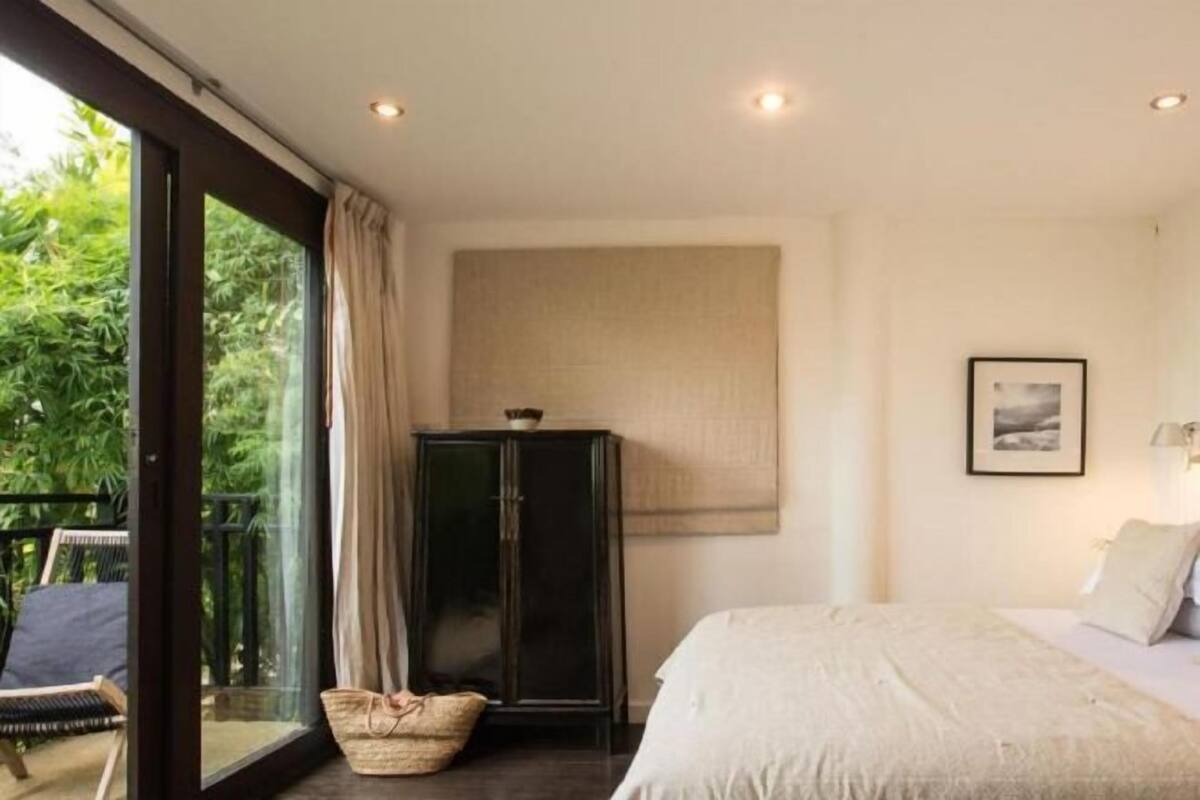 Een slaapkamer met een groot raam, een bed, een kast en een stoel.