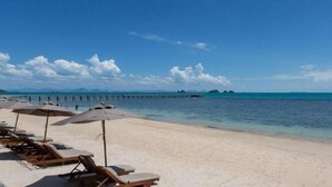 Ein Strand mit Liegestühlen und Sonnenschirmen, eine Seebrücke, die sich ins Wasser erstreckt, und strahlend blauer Himmel.