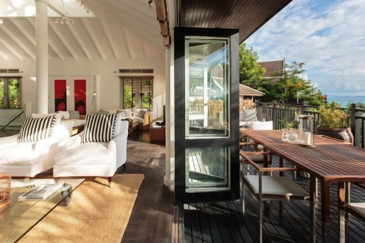 A modern living area with a sofa, a wooden table, and a large glass door leading to an outdoor deck.