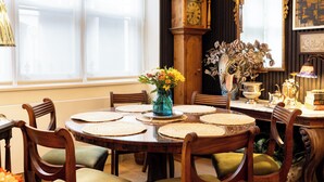 Une salle à manger avec une table en bois, des chaises, un vase de fleurs, une horloge et un miroir.