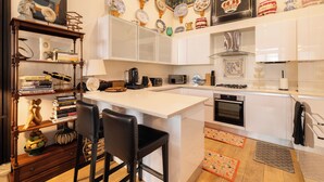 Une cuisine moderne avec des meubles blancs, un îlot central, des tabourets de bar, une bibliothèque et des assiettes décoratives accrochées au mur.