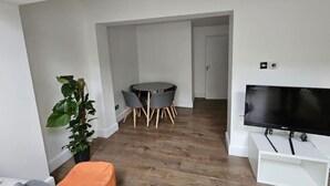 Een moderne woonkamer met een flatscreen televisie, een eettafel met stoelen en een potplant.