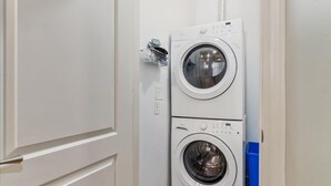 A laundry room with two stacked front-loading washing machines and a blue trash bin. - Quiet spacious apartment  sleeps 4. 1br plus den. (Albany)