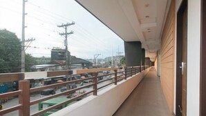 A corridor with a wooden railing, a view of a busy street with vehicles and power lines, and a building with a wooden facade. - RedDoorz @ Traveler Inn Matina (Davao City)