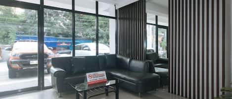 Un área de recepción con un sofá de cuero negro, una mesa de centro de vidrio y una pared con rayas verticales.