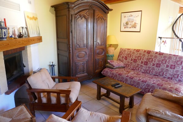 A living room with a sofa, armchairs, a wooden cabinet, and a fireplace.