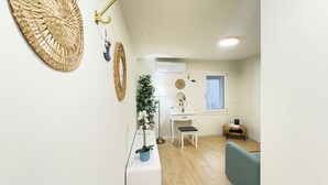 Une pièce avec une coiffeuse blanche, un miroir, une petite table avec une lampe, une plante en pot et une fenêtre donnant sur un beau paysage.